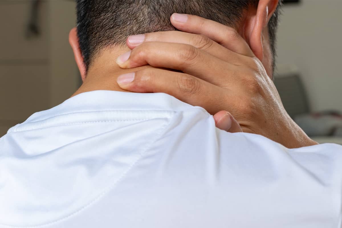 A man from behind touching the back of his neck and scalp, indicating the area where early-stage acne keloidalis nuchae symptoms like small, itchy bumps often appear.