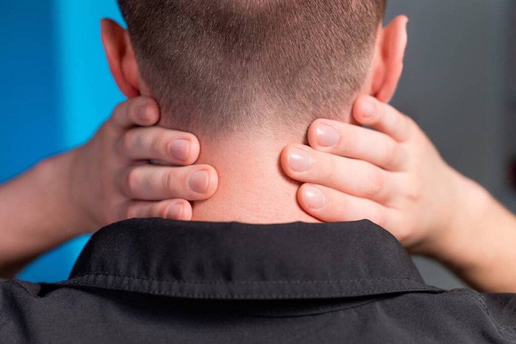 A man seen from behind holding the back of his neck with both hands, highlighting a clear hairline after successful management of a scalp condition.